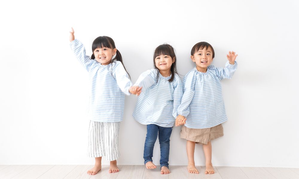 3人の子どもが並んで笑顔で手を上げる
