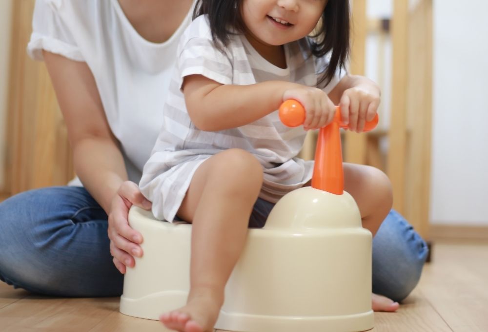幼い子どもがおまるに座り、大人に支えられて笑顔を見せている
