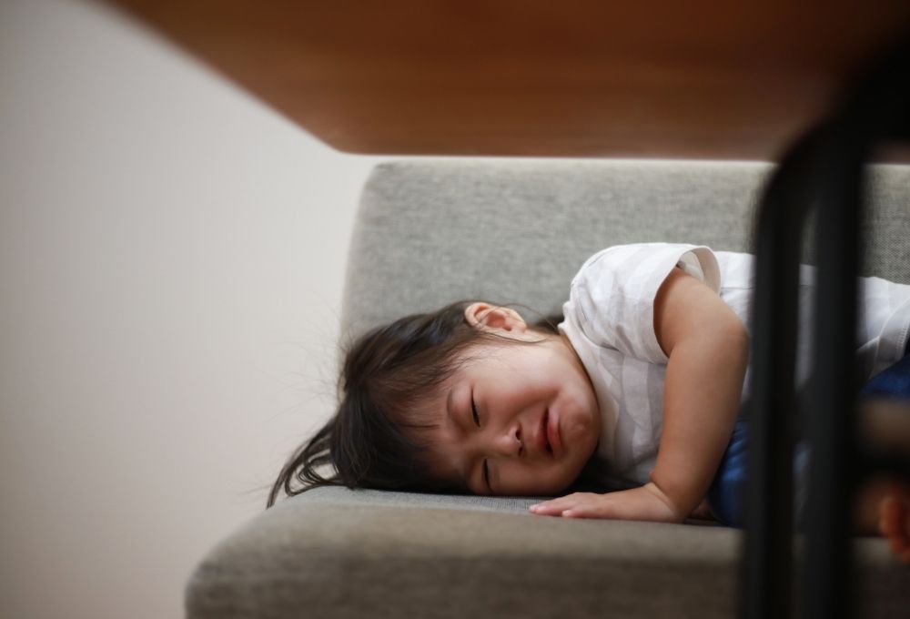 ソファの上で泣きながら横たわる幼児
