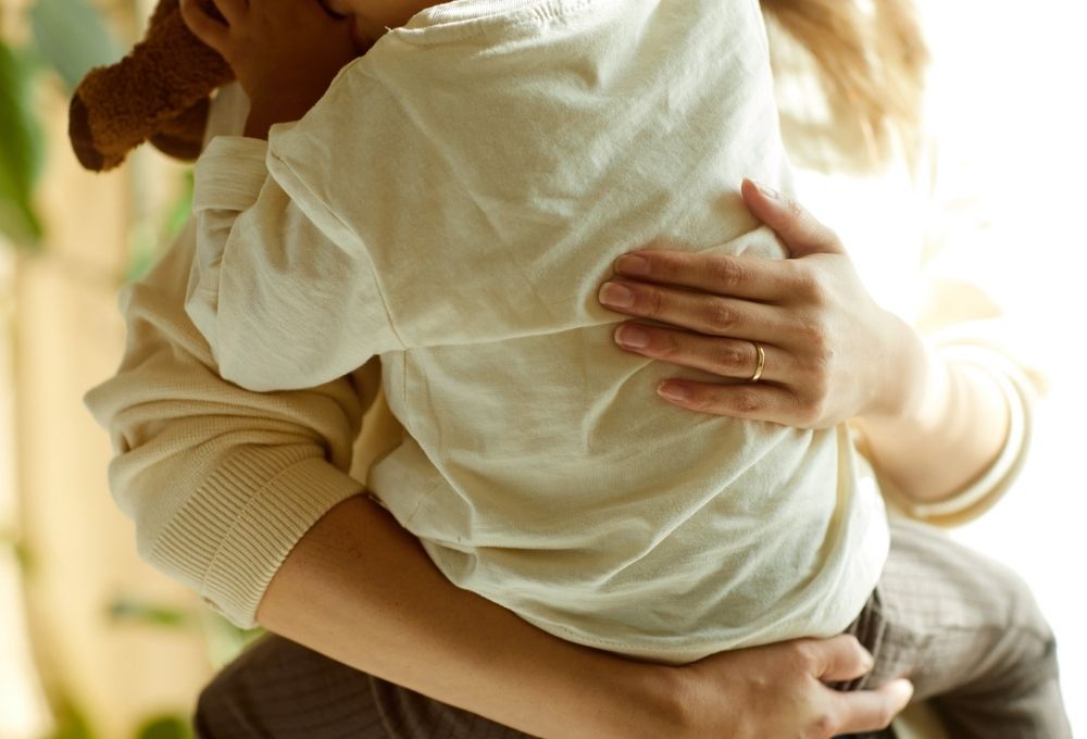 母親にしっかり抱きしめられる子どもの後ろ姿