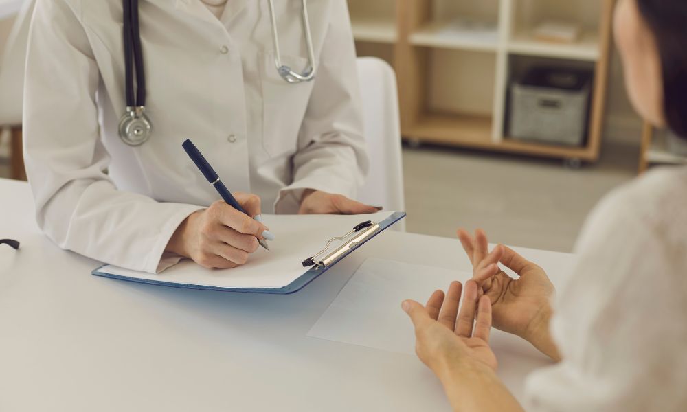 白衣の医師がカルテにメモを取りながら、保護者と相談している様子。