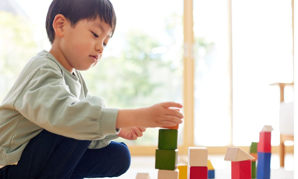 床に座った子どもが、積み木を積み上げながら集中して遊んでいる様子