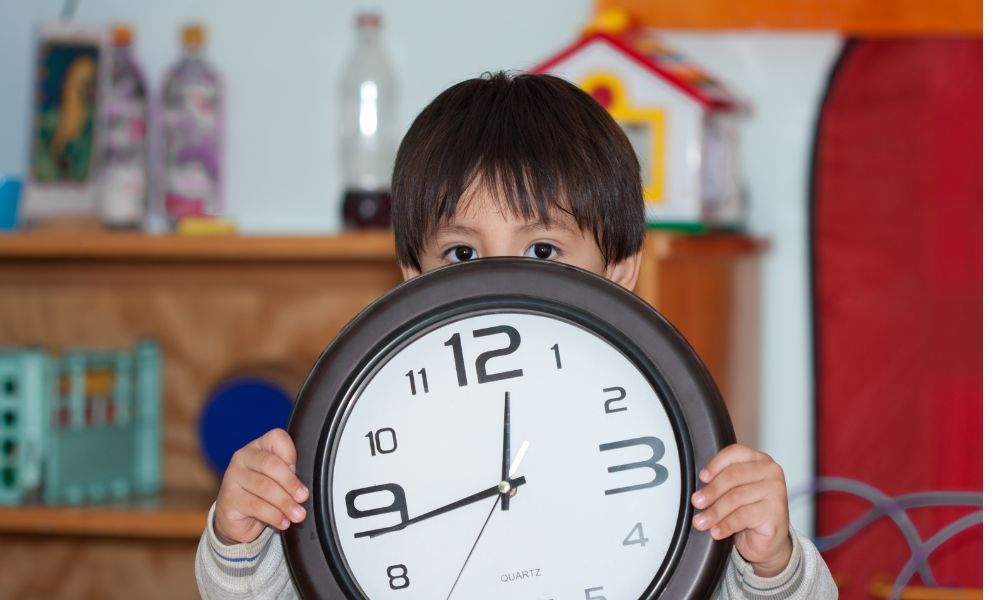 大きな壁掛け時計を子どもが正面から持ち、時計の半分ほど顔が隠れている
