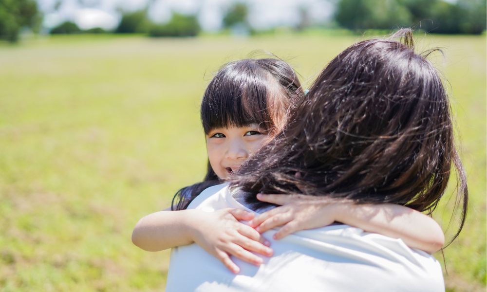 屋外で女の子が大人に抱きしめられ、安心した表情を浮かべている