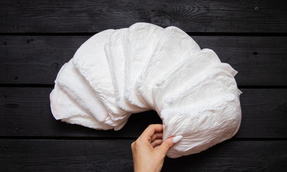 黒いテーブルの上に白いオムツが扇のように並べられ、手が1枚を持ち上げている様子