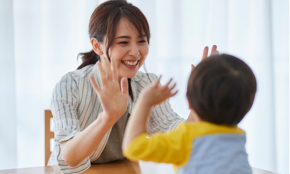 テーブルで向き合い、親子が笑顔でハイタッチしている様子