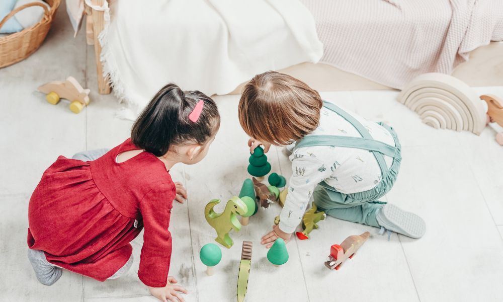 床に座った2人の子どもが木製のおもちゃを並べて遊んでいる様子