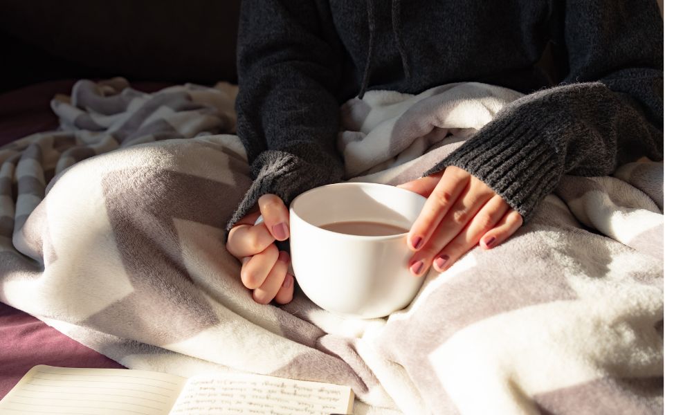 毛布にくるまり、温かい飲み物でほっと一息つく様子。