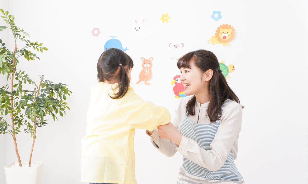 保育士が笑顔で子どもの手を取り、やさしく話しかけている様子