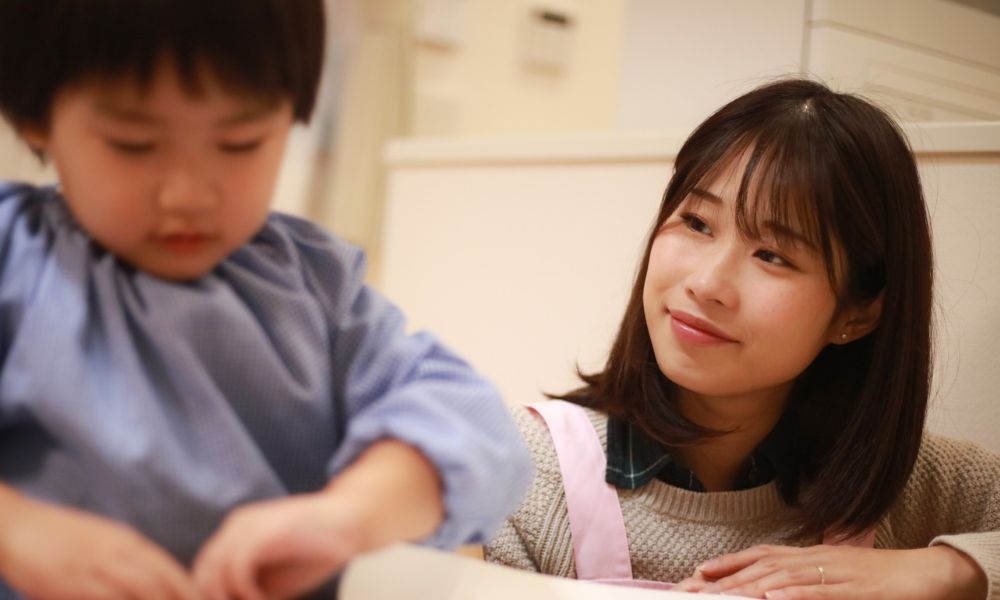 保育者が優しい表情で子どもを見守り、子どもが作業に集中している様子