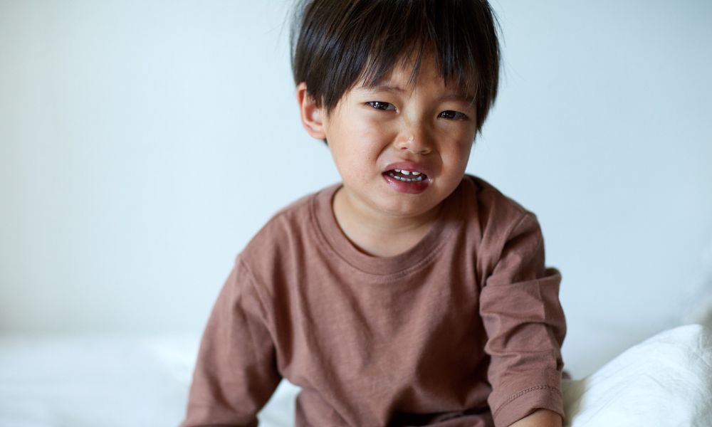 ベッドの上で、泣きそうな表情で座っている男の子