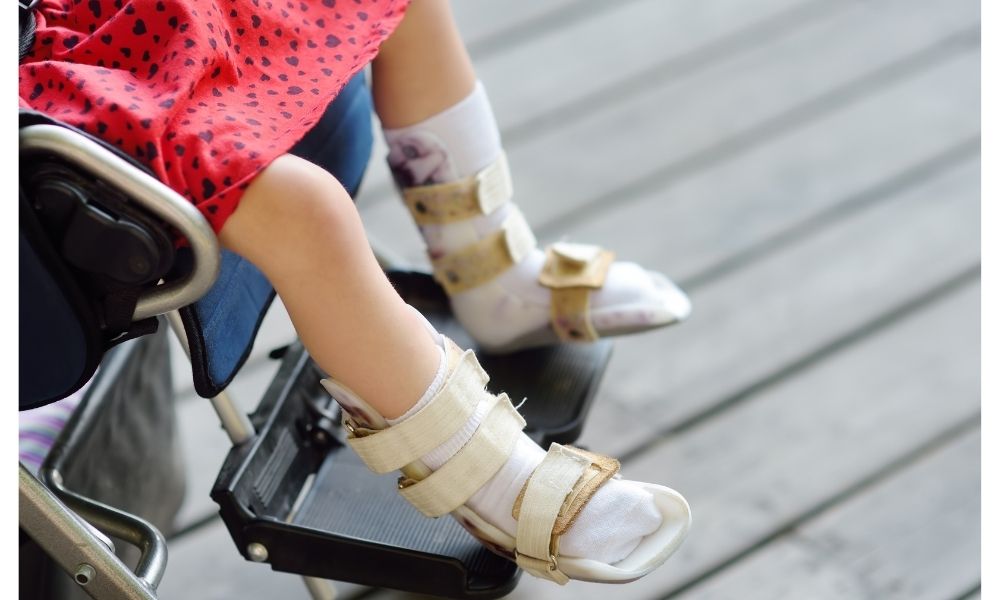 車いすに座る子どもの足元を写した写真で、両足に装具を装着している様子が見える。医療的ケアやリハビリ、日常生活を支える支援の一場面を伝えるイメージ。