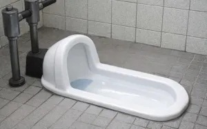 床に埋め込まれた和式トイレが写っています。前に向かってしゃがんで使用する形で、周囲はタイル張りの床と配管が見える構造です