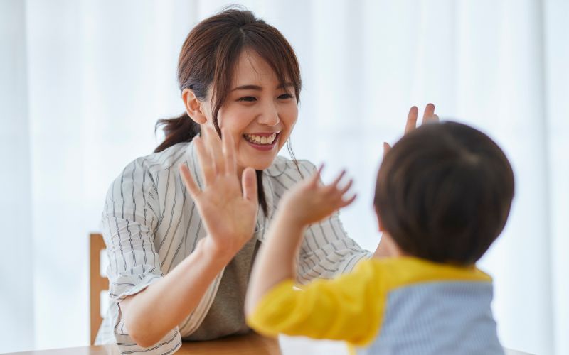 向かい合った大人と子どもが、笑顔で手を合わせて喜びを共有している様子。できたことを認め、成功体験をポジティブに強化している場面を写した写真