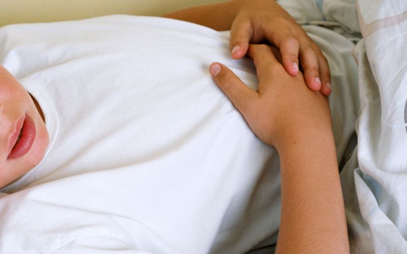 子どもが仰向けに寝て、お腹に手を当てています。お腹の不快感や違和感を感じている様子を示しています