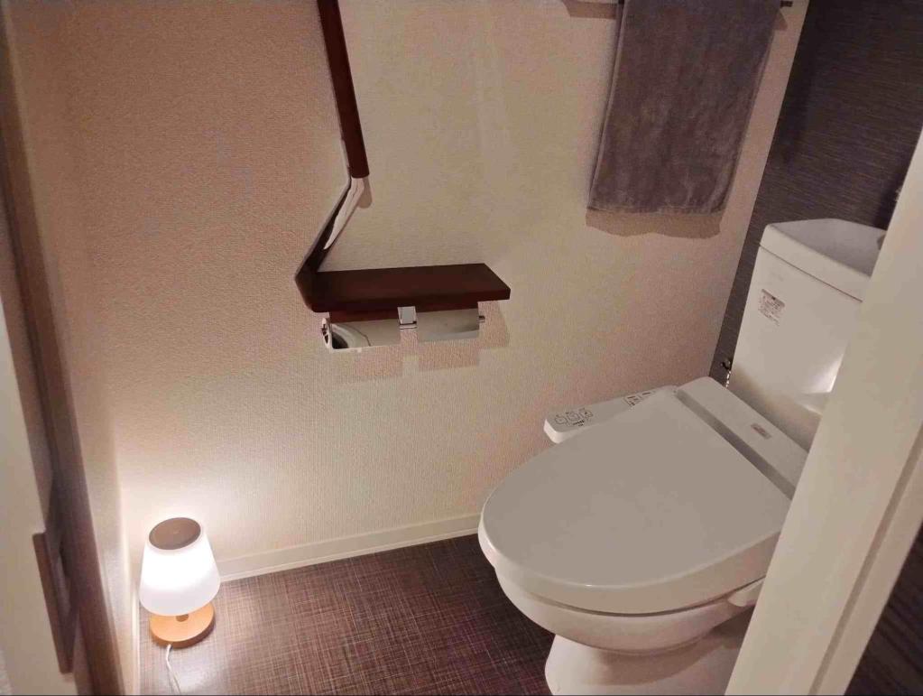 トイレの床に小さな間接照明が置かれ、やわらかい光で空間が照らされている様子。落ち着いた雰囲気の中で、手すりやトイレットペーパーも見える