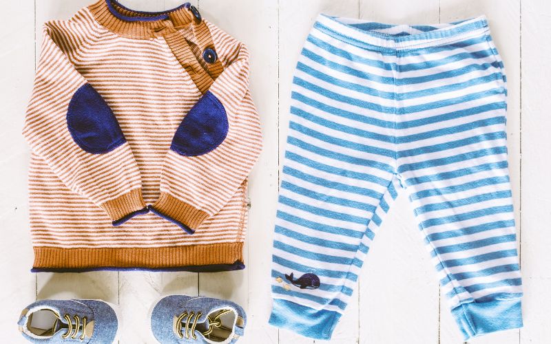白い木の床の上に、子どもの服がコーディネートされた状態で並べられている写真。ボーダー柄のセーター、青いボーダーのズボン、小さな靴が整えて配置されている