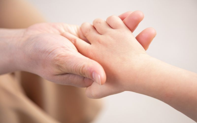 大人の手が子どもの手を優しく握って支えている様子。安心感やサポートを感じさせる場面。