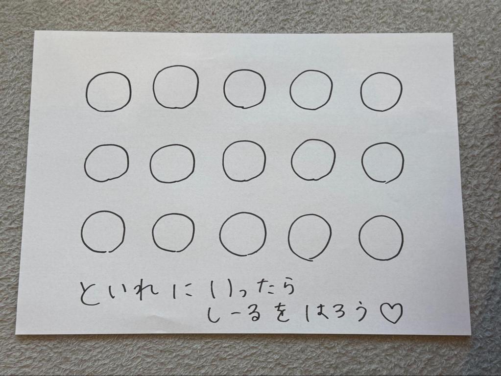 白い紙に手書きの丸が規則的に並んでおり、下部に「といれにいったら しーるをはろう♡」と書かれている。トイレに行けたらシールを貼るためのご褒美シート。
