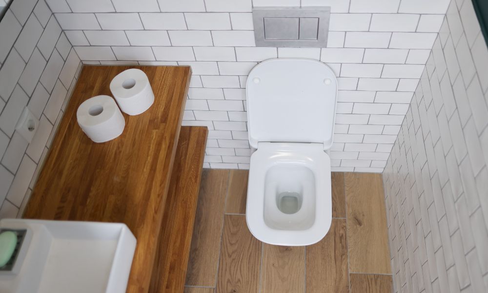 上から見下ろしたトイレ空間の写真。白い便器と木目調の棚、トイレットペーパーが配置され、シンプルで整理されたトイレ環境や排泄スペースをイメージさせる構図。
