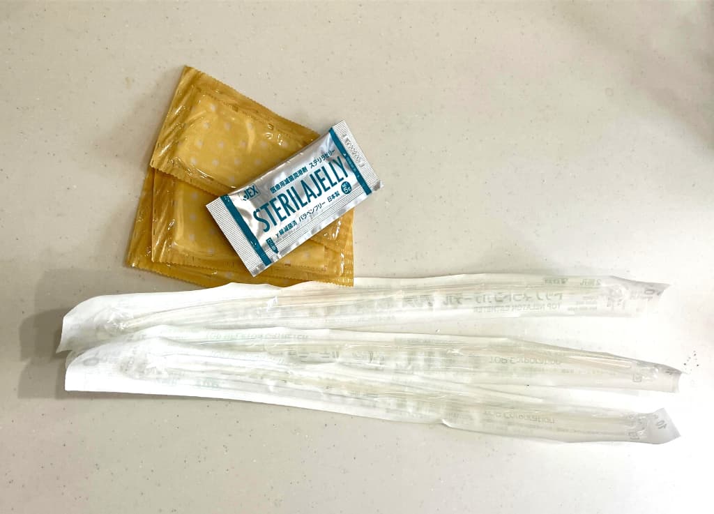 自己導尿に使用する医療用品が並べられた写真。個包装のカテーテル、潤滑ゼリー、使い捨て手袋が配置されており、自己導尿の準備や必要物品をイメージさせる構図。