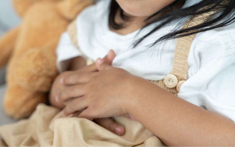 腹部を押さえて不快そうに座る子ども